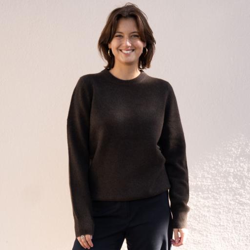 Flauschig warme Pullover und Jacken für Damen und Herren Frau in dunklem Pullover vor beiger Wand